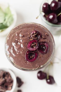 a chocolate dessert with cherries on top and other fruit in bowls behind it,