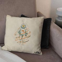 a pillow with an astronaut on it sitting on a couch next to a vase and lamp