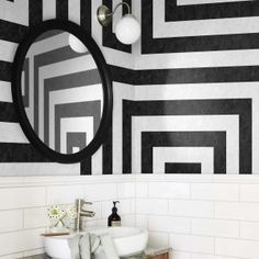 a bathroom with black and white tiles on the wall next to a sink, mirror and vanity