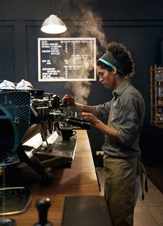 a woman is working on an espresso machine in a coffee shop with steam coming out of it