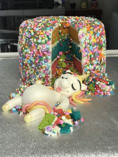 a cake with sprinkles and a unicorn laying on the ground next to it