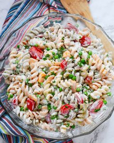 a pasta salad with tomatoes, peas and parsley in a glass bowl on a striped cloth