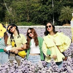 three young women standing in a field of purple flowers wearing yellow jackets and sun glasses