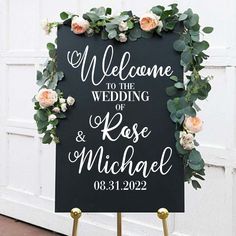 a welcome sign with flowers and greenery on it in front of a white door