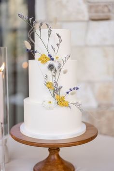 a white wedding cake with yellow and purple flowers on the top is sitting on a wooden stand