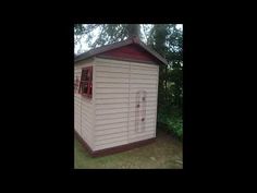 a small white shed sitting in the middle of a yard next to trees and bushes