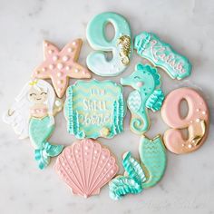 decorated cookies arranged in the shape of mermaids and seashells on a marble surface