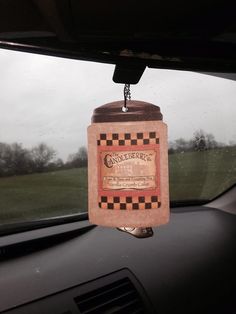 a bottle hanging from the dashboard of a car in front of a window with grass and trees behind it