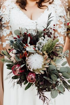 a bride holding a bouquet of flowers and greenery in her hands, wearing a lace wedding dress