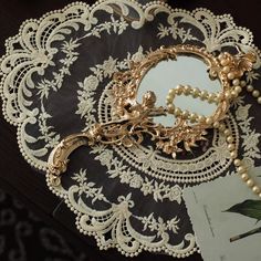 an ornate mirror with pearls on it sitting on top of a lace doily next to a brooch