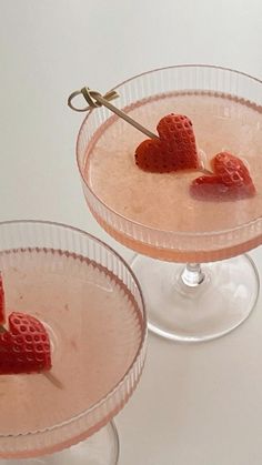 two martinis with strawberries in them on a white counter top and one has a heart shaped stick sticking out of it