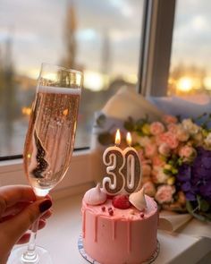 someone holding a wine glass near a pink cake with the number 30 on it and candle