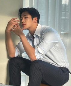 a young man sitting on top of a bed next to a window in a room