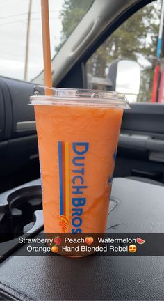 an orange drink sitting on top of a table next to a black car door window