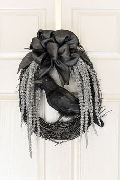 a black bird sitting on top of a wreath hanging on a white door with silver beads