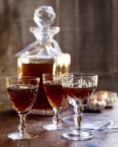 three glasses filled with liquid sitting on top of a table next to a decanter