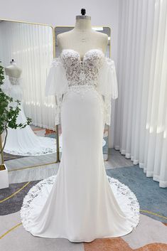 a white wedding dress on display in front of a mirror and mannequins