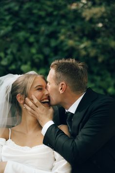 the bride and groom are kissing each other in front of some greenery on their wedding day