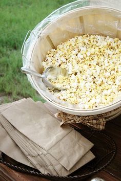 a bowl filled with popcorn sitting on top of a wooden table next to napkins