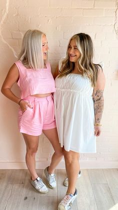 two women standing next to each other in front of a brick wall and wearing pink shorts