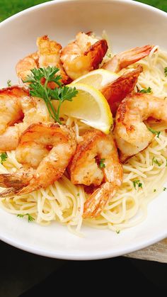 a white bowl filled with pasta and shrimp on top of a wooden table next to a lemon wedge