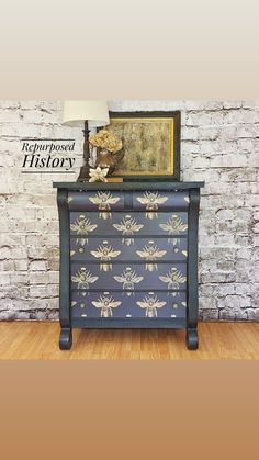 an old dresser with flowers painted on it and a lamp next to it in front of a brick wall