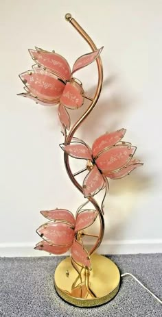 a metal sculpture with pink flowers on it's side and a gold plated base