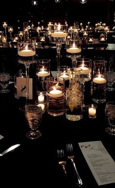 many candles are lit in glass vases on a table with silverware and menu cards