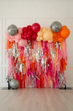 an assortment of balloons and streamers on a wall in front of a disco ball