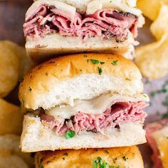 three pastrami sandwiches stacked on top of each other next to some potato chips