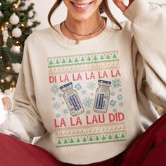 a woman sitting in front of a christmas tree wearing a sweater with two jars on it