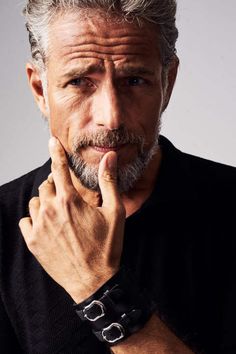 a man with grey hair and beard wearing a black shirt is posing for the camera