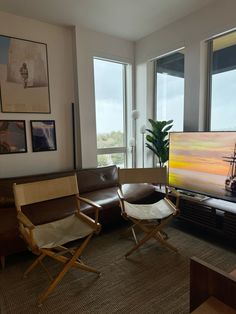 a living room with two chairs and a large painting on the wall above it's windows