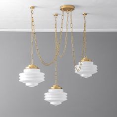 three light fixtures hanging from the ceiling in a room with gray walls and gold chains