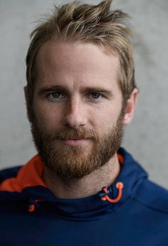 a man with a goatee and beard wearing an orange and blue hoodie looking at the camera