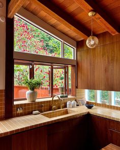 a kitchen with wooden cabinets and tile counter tops, along with a large window that looks out onto the trees outside