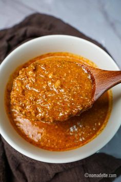 a wooden spoon in a white bowl filled with chili sauce on top of a brown napkin