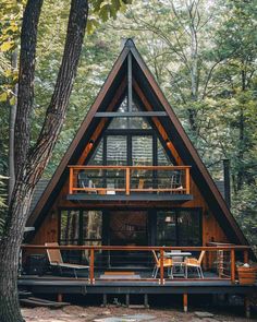 a - frame cabin in the woods with deck and chairs on the front porch, surrounded by trees