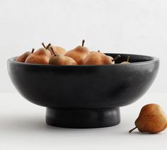 a black bowl filled with pears on top of a white table