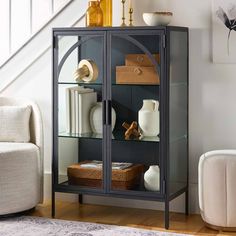 a bookcase with glass doors and shelves in a living room area next to a white chair