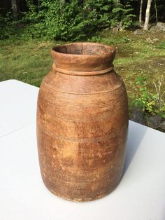 a brown vase sitting on top of a table in front of some grass and trees