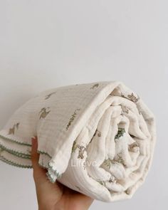 a hand holding up a white blanket with green trimmings on the bottom and sides