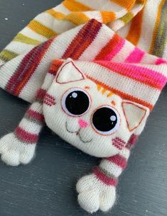 a knitted cat with big eyes and a striped scarf on it's head