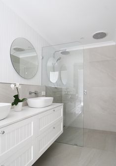 a white bathroom with two sinks and a large mirror on the wall next to it