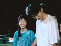 a man and woman standing next to each other in front of a car at night