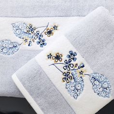 two white towels with blue and yellow flowers on them, sitting next to each other