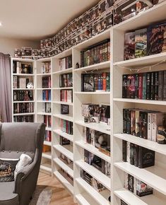 a living room filled with lots of white bookshelves next to a gray chair