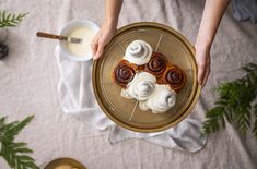 a person holding a plate with pastries on it next to coffee and pine cones