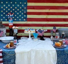 an american flag themed picnic table set up with patriotic food and desserts on it