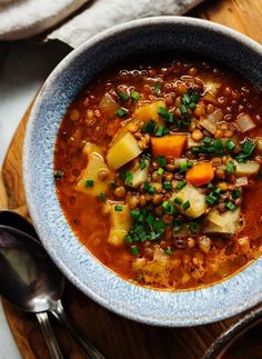 a bowl filled with soup and vegetables on top of a wooden table next to spoons